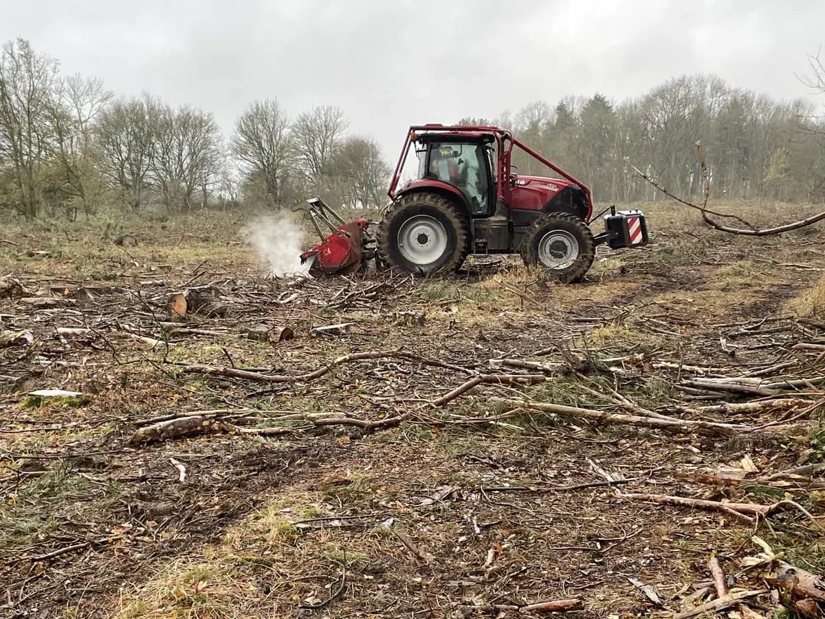 Forestry tractor's mulching head throwing chips as it clears felled woodland