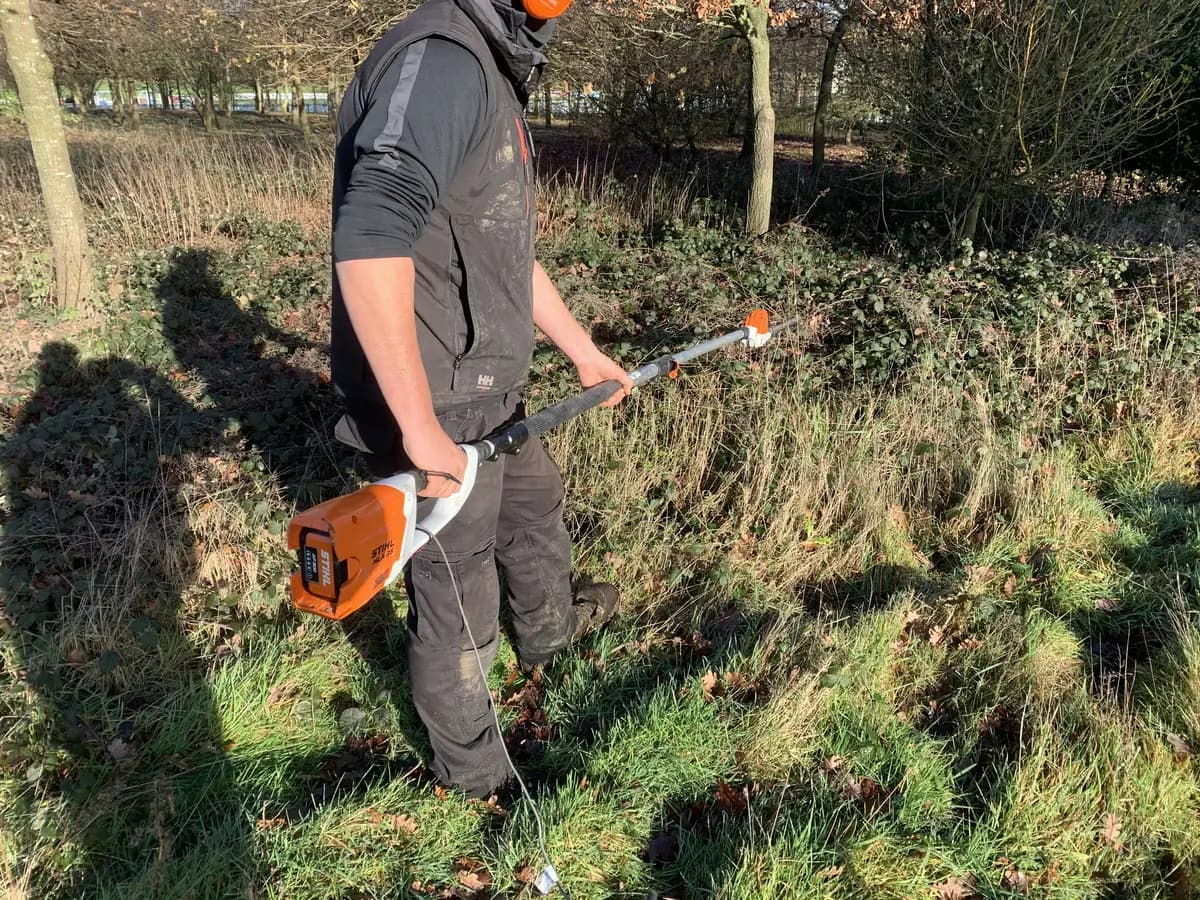 Long-reach hedge trimmer with a wired vibration sensor, clearing scrub on rough ground