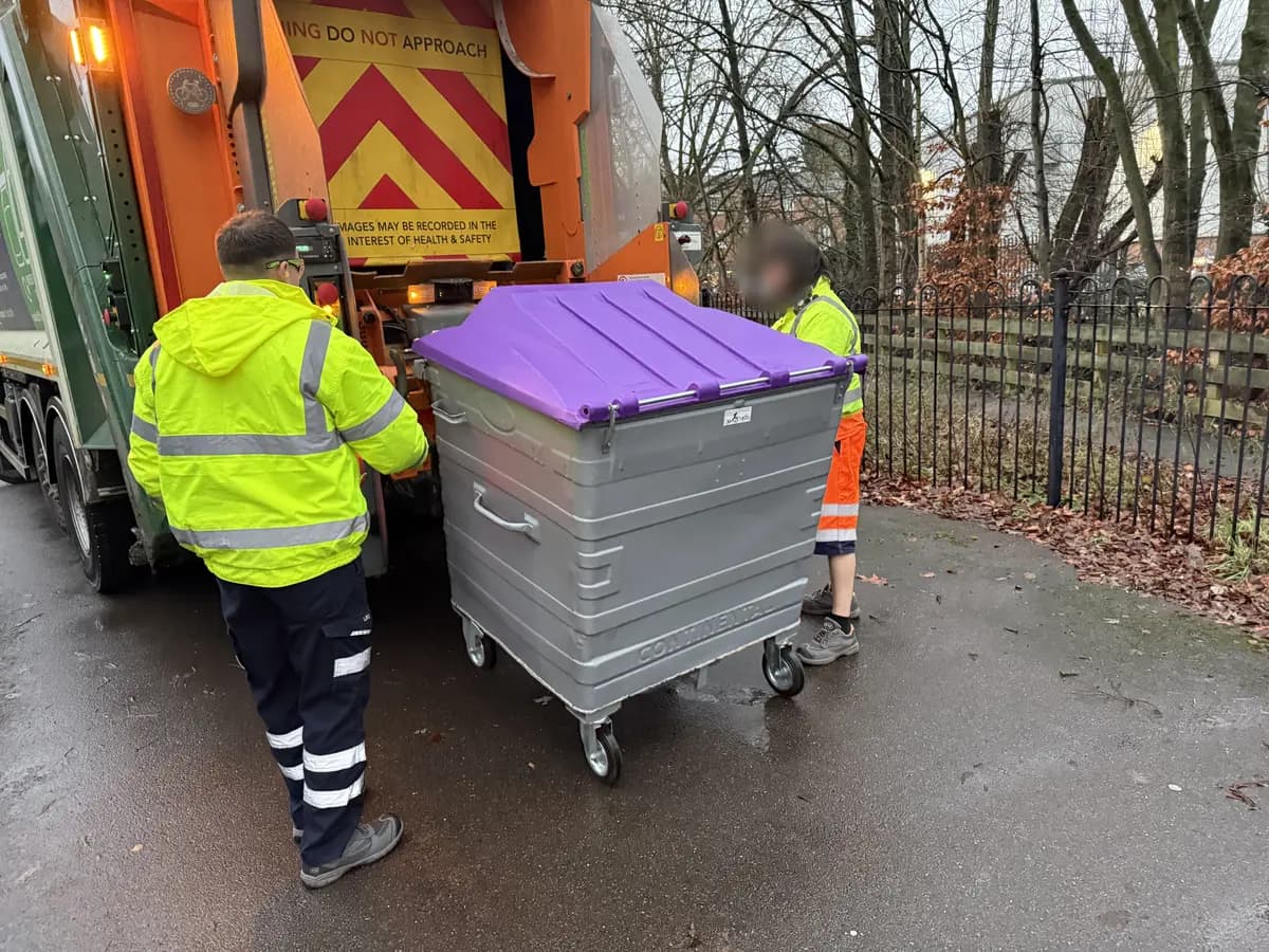 Refuse crew wheeling a communal bin onto the lift of a collection vehicle