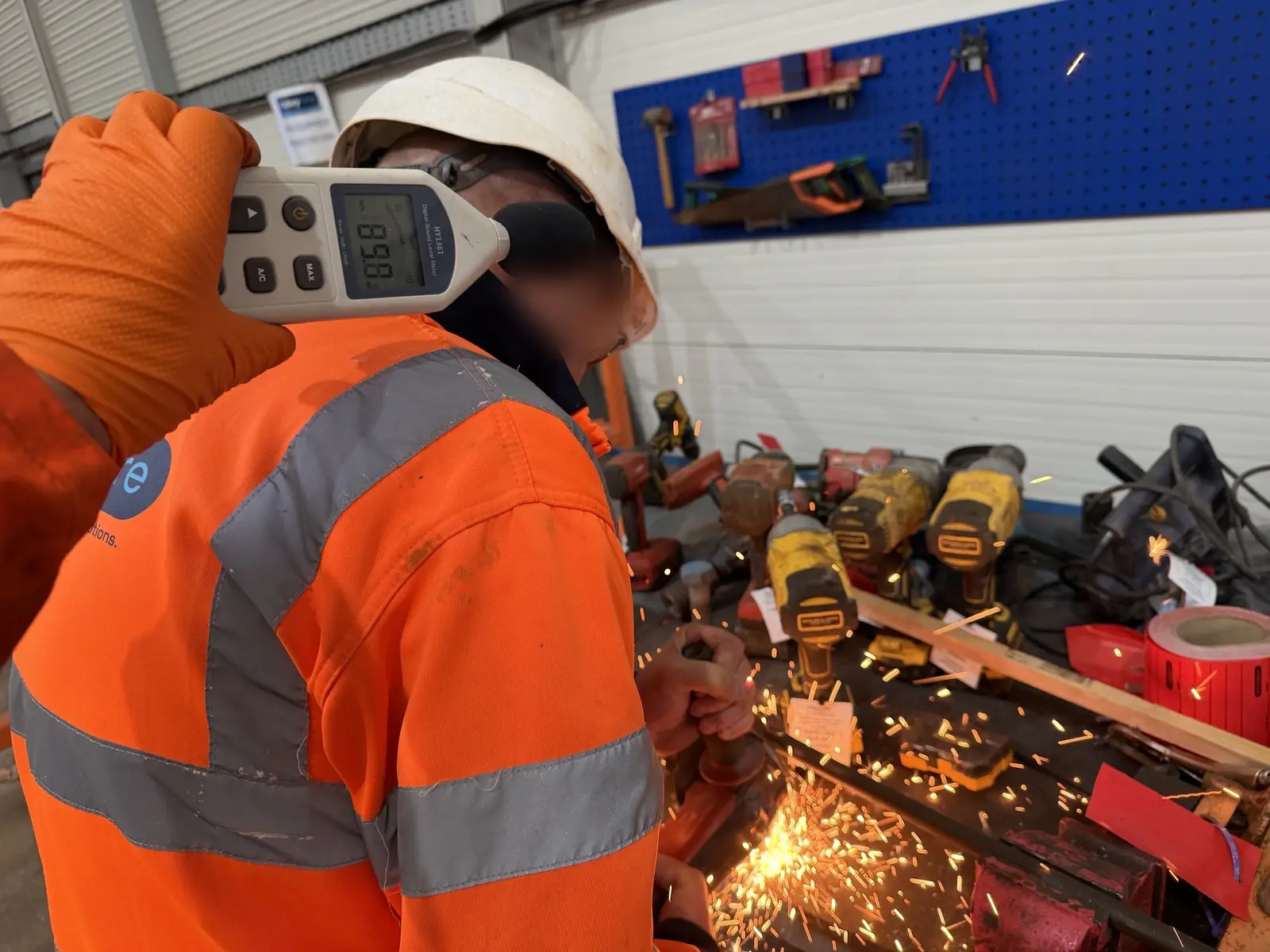 Sound level meter at the operator's ear reading 89.8 dB as he cuts metal at a workshop bench, sparks flying
