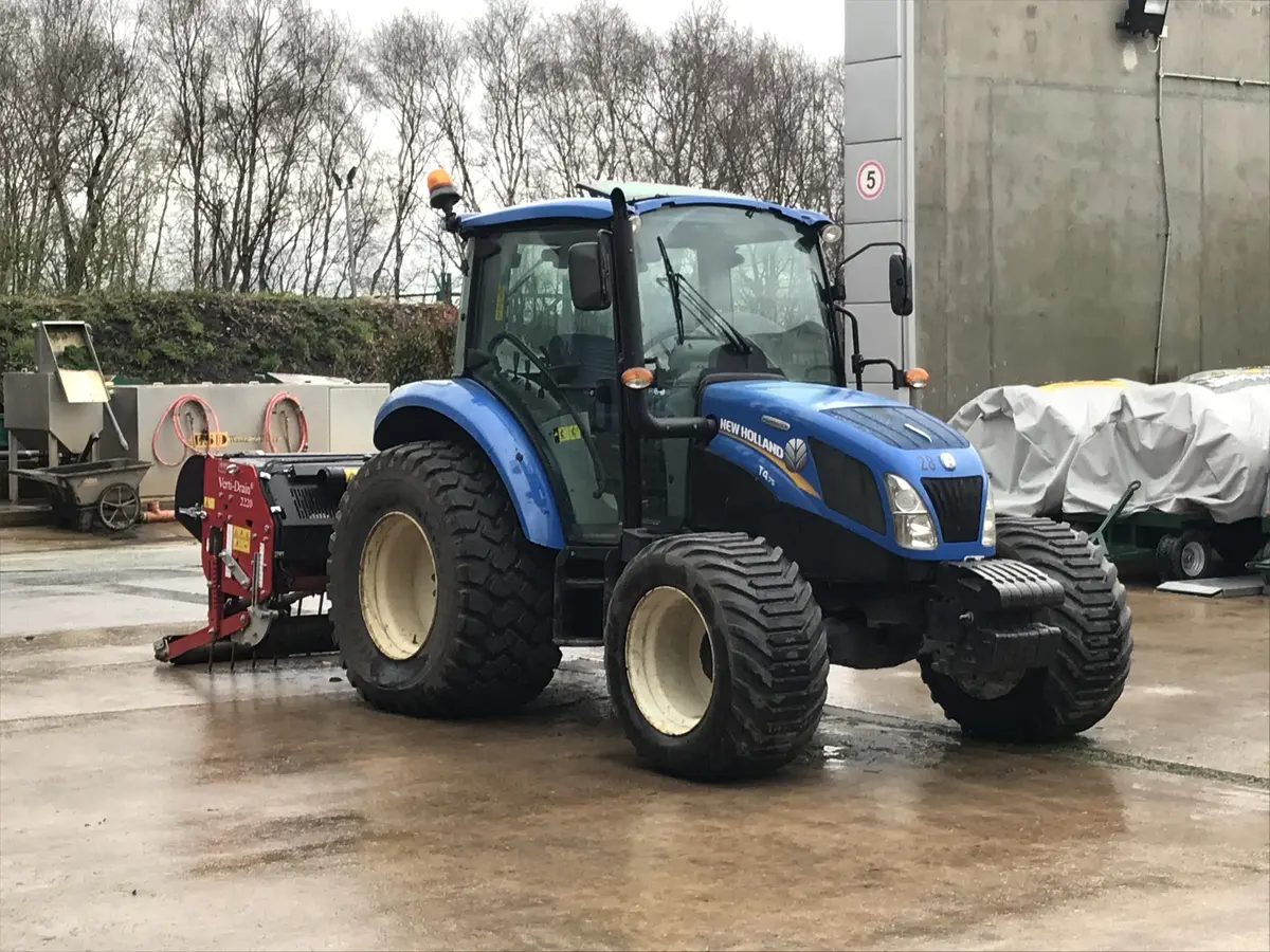 Compact tractor with a deep-tine aerator mounted, parked in a wet yard