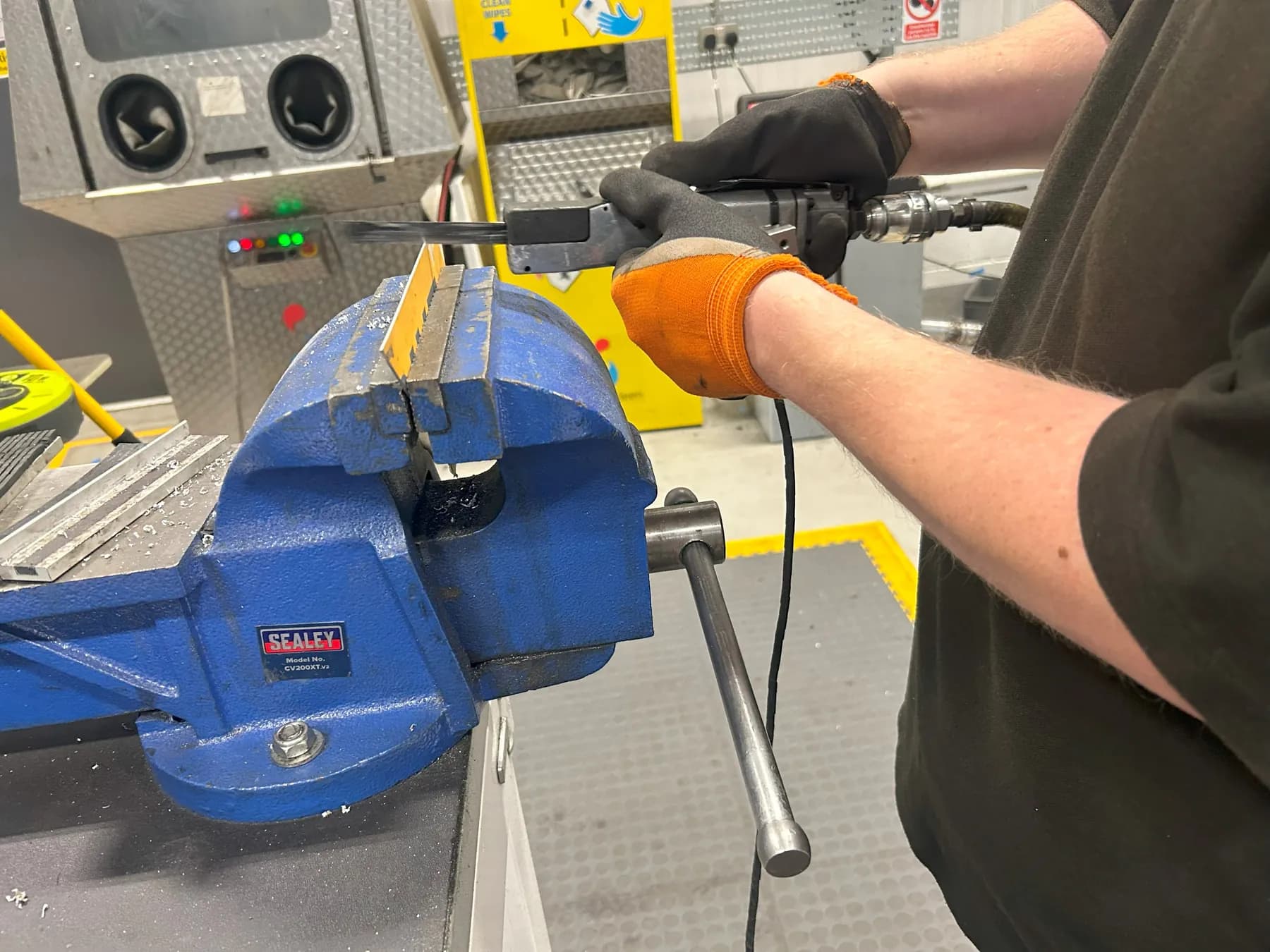 Fitter in gloves testing an air-powered tool at a bench vice in the vehicle workshop